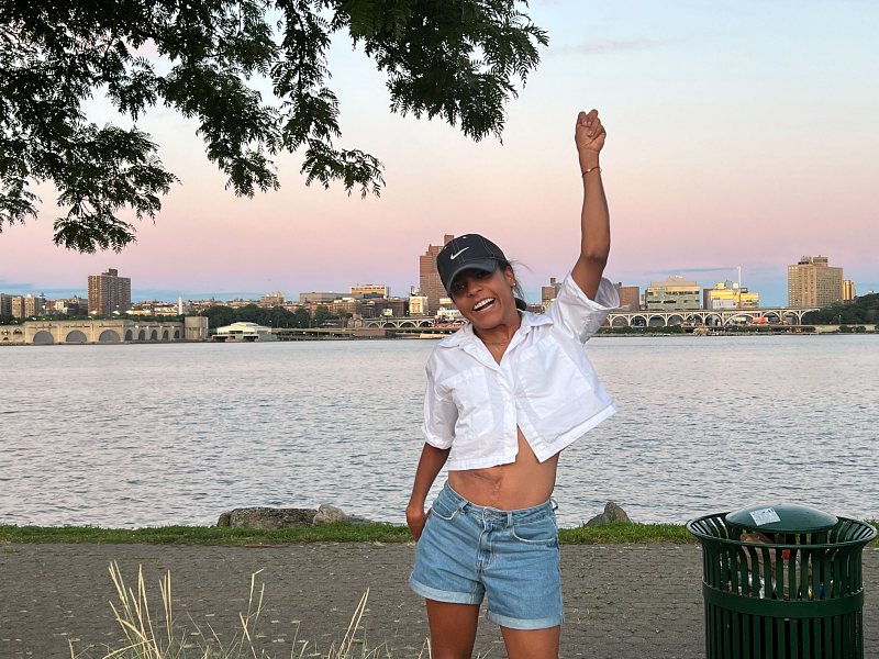 Take it or leave it- Latina wearing blue jean short and a white crop button down to and cap and green converse raising left hand up