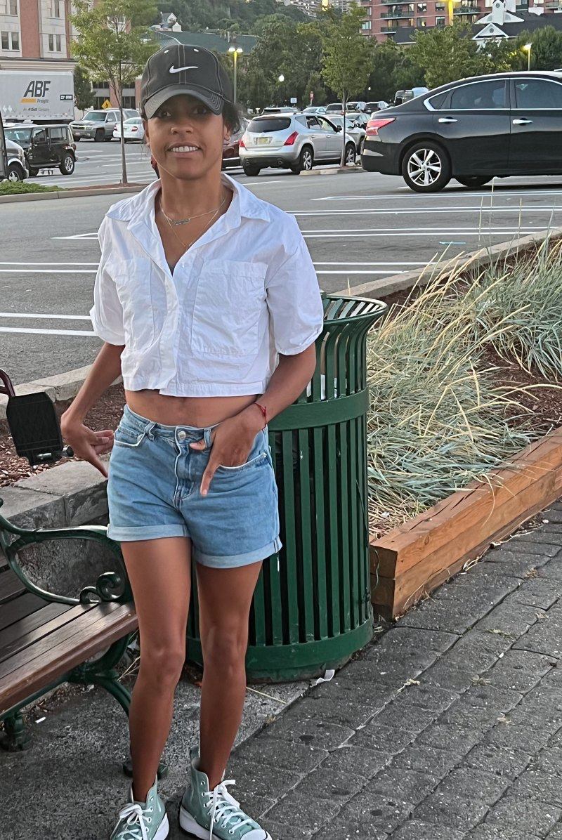 Take it or leave it- Latina wearing blue jean short and a white crop button down to and cap and green converse